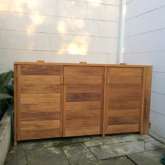 Bespoke triple wheelie bin store crafted from natural hardwood featuring horizontal slatted doors, installed in a flagstone courtyard.