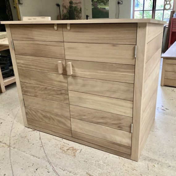 Bespoke hardwood outdoor storage cupboard with horizontal timber slats and custom wooden handles, shown inside a joinery workshop.