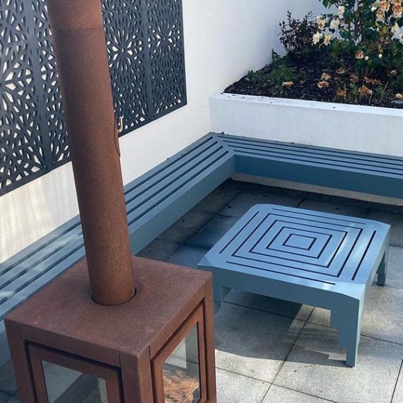 Art deco style slate blue accoya floating wooden corner bench integrated into a white rendered garden wall, featuring a matching geometric low table.