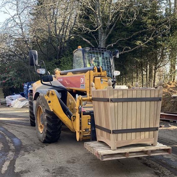 Large bespoke tapered hardwood Trinity Versailles planter with metal braces being transported on a forklift, in private Surrey Estate.