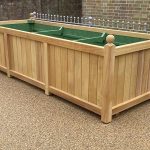 Extra large bespoke hardwood trough planter with natural timber finish, traditional panelled sides and decorative ball finials.