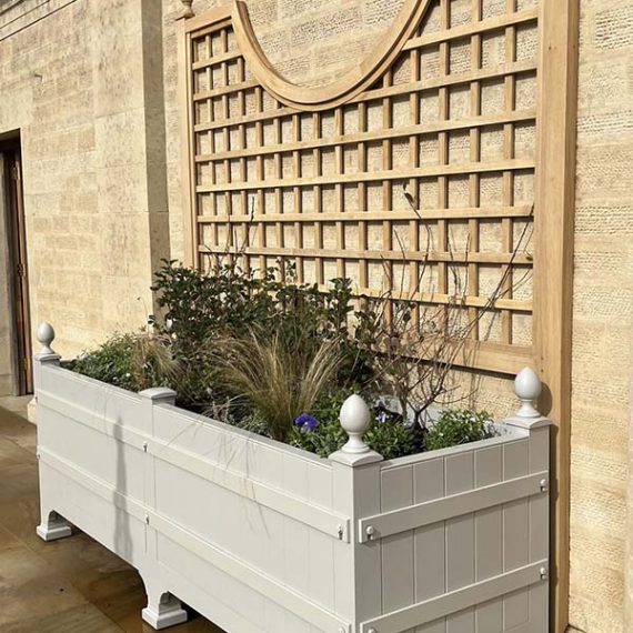 Bespoke cream Churchill Versailles wooden trough planter beneath decorative oak trellis at a private country estate.