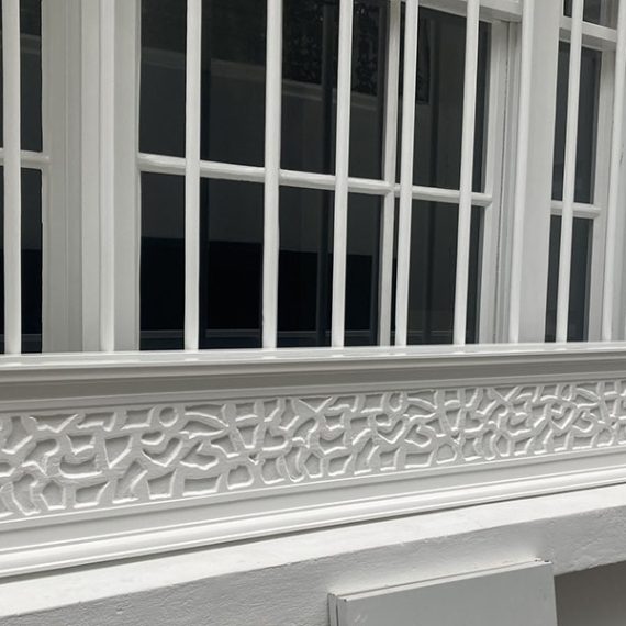 Narrow white wooden window box planter featuring a textured rusticated masonry pattern sitting on the exterior sill of a London townhouse window.