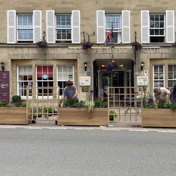Bespoke natural hardwood trough planters with slanted bases, positioned outside a traditional stone-fronted building.