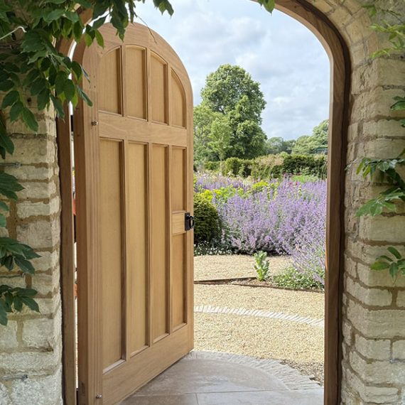 Bespoke replication of a luxury Georgian arched hardwood estate gate, handcrafted in a classical period style with multi-panel oak joinery, opening to a formal walled garden.
