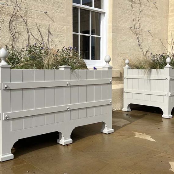Pair of bespoke cream Versailles-style Accoya wooden trough planters with decorative finials outside a stone building