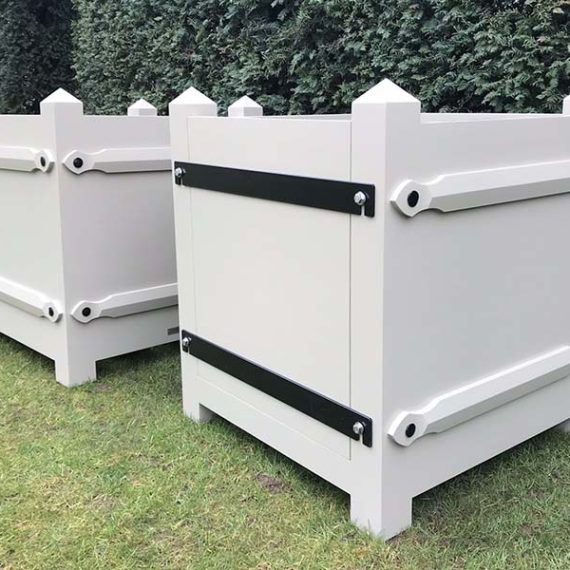 Bespoke made-to-order Versailles style Accoya planters featuring a removable side panel with heavy black structural ironmongery braces, pyramid finial corner posts, and a flawless off-white painted finish on an estate lawn.