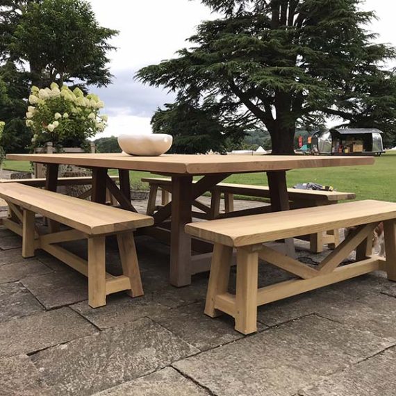 Luxury round wooden garden dining table set with slatted carver armchairs and matching wooden stool on a grey decked patio
