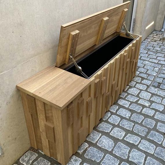 Art Deco style oak bespoke wooden outdoor storage unit with a hinged lid held open by metal struts, showcasing a textured and stepped geometric block pattern.