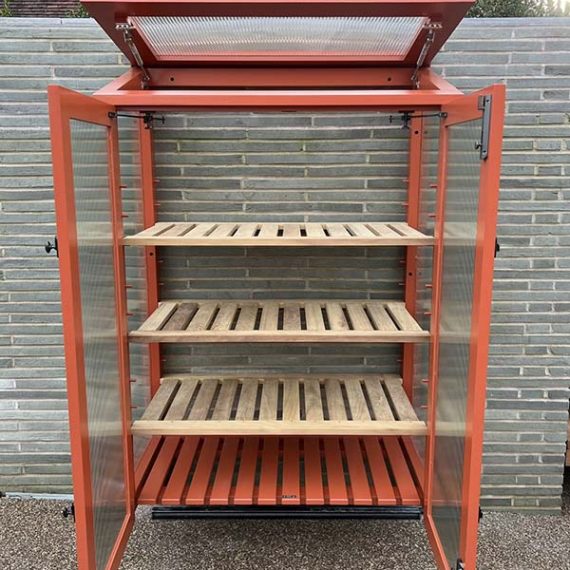 Bespoke freestanding upright coldframe painted terracotta orange with fluted glass doors and an open top lid, showcasing three natural wood slatted plant shelves against a modern grey brick wall.