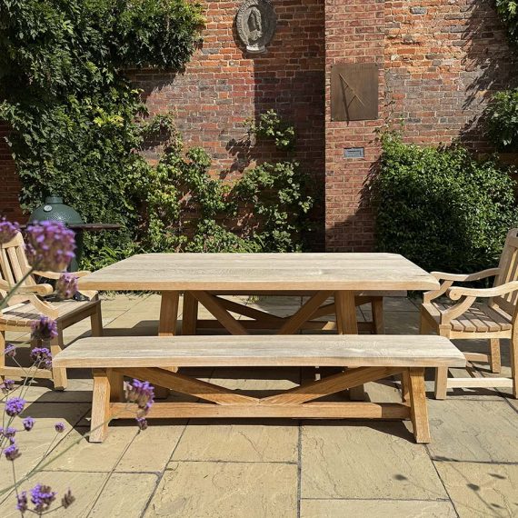 Bespoke grand hardwood outdoor dining table set with a matching cross-frame bench and two carver armchairs on a paved courtyard patio