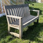 Silvered three seater bespoke oak bench with a slanted backrest and rounded slatted base.