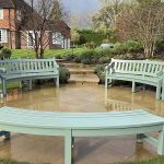 Durable bespoke hardwood garden seating set featuring curved sage green benches and matching side tables on a circular terrace.