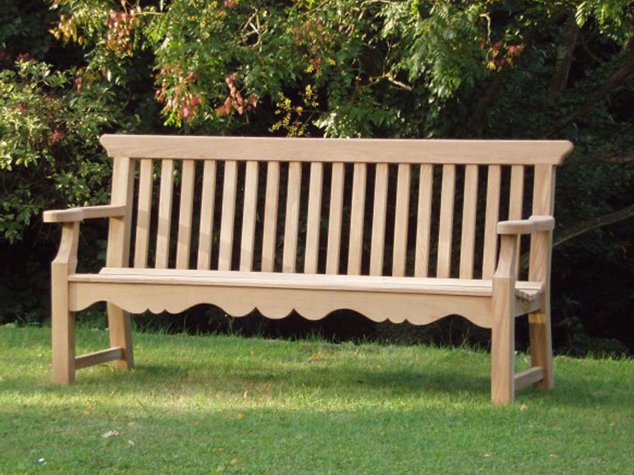 Handcrafted solid English oak garden bench with a decorative scalloped apron and slatted back on a formal lawn.