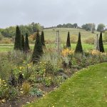 Handcrafted sage green timber tuteurs featuring traditional cross-treillage joinery and spherical finials set in a luxury country estate border.