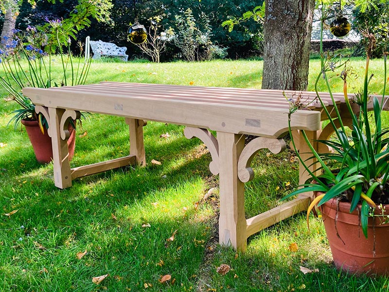 Handcrafted backless oak garden bench in Arts and Crafts style featuring curved support brackets and spherical finials.