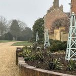 Pale sage green timber garden obelisk with cross-lattice framing and ball finial.