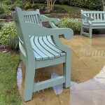 Close-up side profile of Dyffryn bespoke hardwood garden bench painted sage green, highlighting the thick timber slats and elegant scrolled armrest detail.