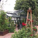 Handcrafted Iroko hardwood obelisk with carved acorn finial supporting climbing roses.